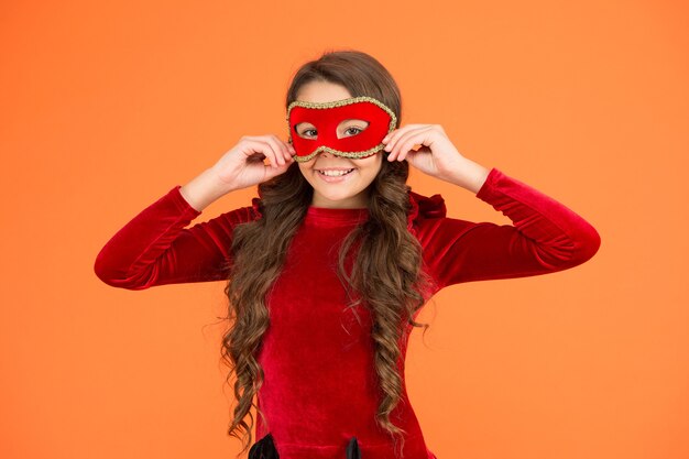 Carnevale invernale. Modalità incognito. I bambini indossano una maschera per gli occhi. Ragazza indossare maschera sfondo arancione. Evento invernale e intrattenimento. Sviluppo del bambino. Visita l'evento pubblico in modo anonimo. Festa di capodanno invernale.