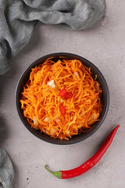 Carota coreana in una ciotola scura su uno sfondo grigio, vista dall'alto del primo piano