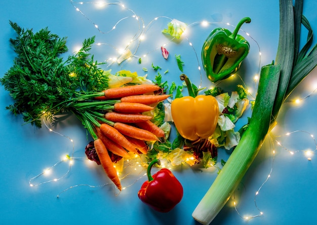 Carota fresca con porri, insalata, pepe e lucine sulla superficie blu