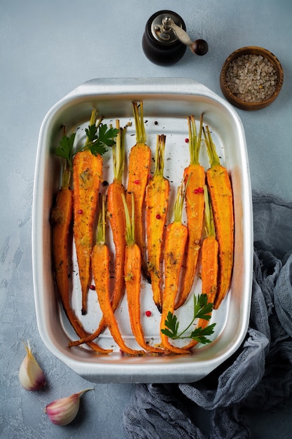 Carote al forno con spezie, aglio e olio d'oliva in una semplice forma di alluminio su un cemento grigio.