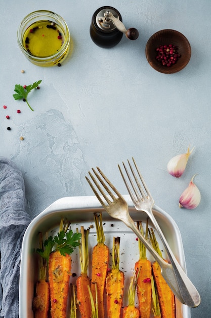 Carote al forno con spezie, aglio e olio d'oliva in una semplice forma di alluminio su un cemento grigio.