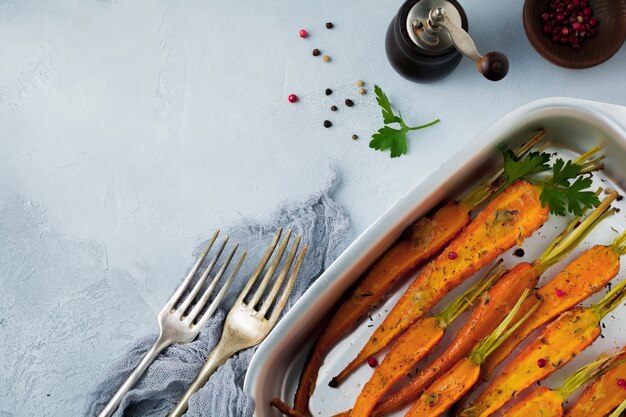 Carote al forno con spezie, aglio e olio d'oliva in una semplice forma di alluminio su un cemento grigio.