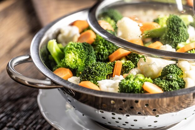 Carote broccoli e cavolfiore cotti al vapore in una vaporiera in acciaio inossidabile con coperchio