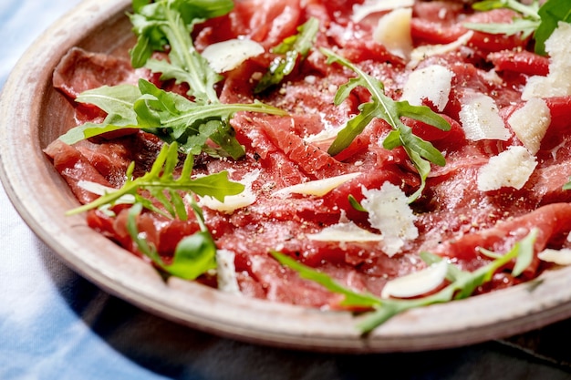 Carpaccio di manzo classico con formaggio e rucola su piatto in ceramica sulla tovaglia bianca e blu.