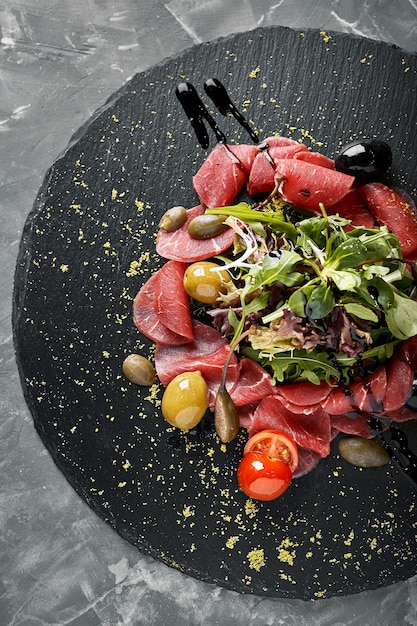 Carpaccio di manzo con rucola su un piatto nero, cucina tradizionale italiana