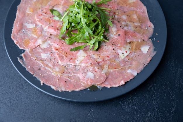 Carpaccio di manzo marmorizzato con rucola parmigiano olio d'oliva e limone Un antipasto classico tradizionale a base di carne cruda affettata sottilmente Primo piano fuoco selettivo vista dall'alto sfondo nero