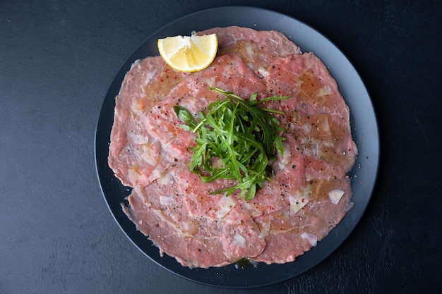 Carpaccio di manzo marmorizzato con rucola parmigiano olio d'oliva e limone Un antipasto classico tradizionale a base di carne cruda affettata sottilmente Primo piano fuoco selettivo vista dall'alto sfondo nero