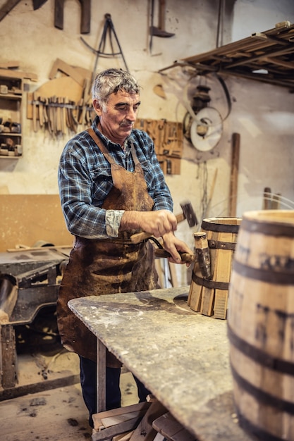 Carpenter mette una striscia di metallo su un nuovo barile di legno realizzato nel suo accogliente laboratorio.