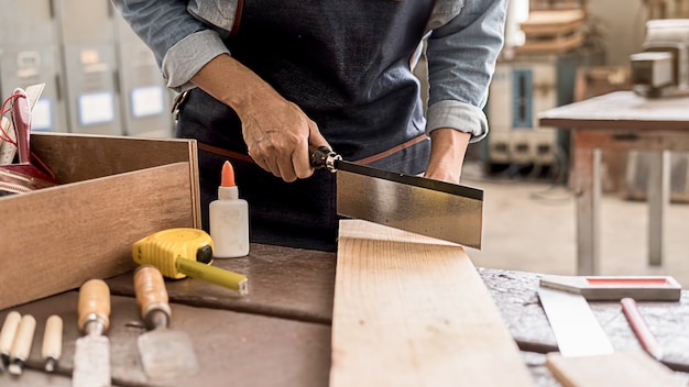 Carpentiere che lavora con l'attrezzatura sulla tavola di legno nel negozio di falegnameria.