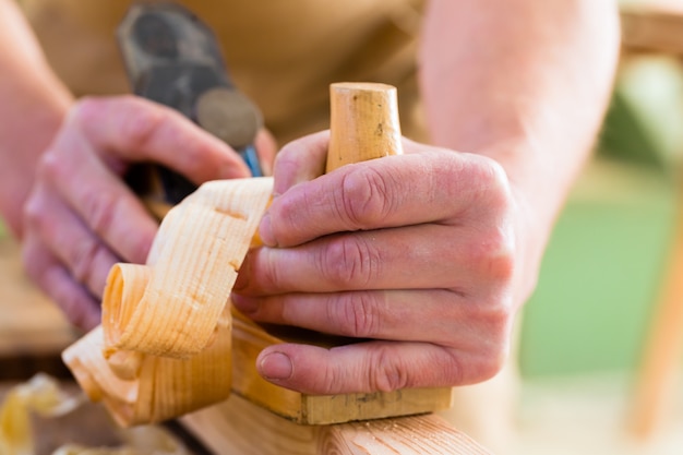 Carpentiere con pialla in legno e pezzo in lavorazione in carpenteria