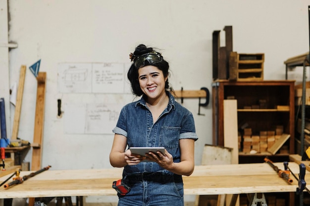 Carpentiere femminile allegra che utilizza una compressa nella sua officina