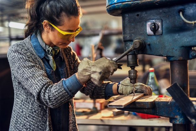 Carpentiere femminile che lavora ad un grande trapano elettrico in officina