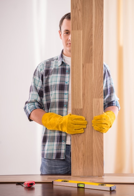 Carpentiere in guanti di gomma che tengono le plance di legno.