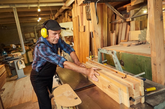 Carpentiere senior in uniforme lavora su una macchina per la lavorazione del legno presso la produzione di falegnameria