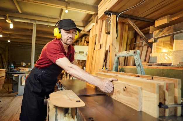 Carpentiere senior in uniforme lavora su una macchina per la lavorazione del legno presso la produzione di falegnameria