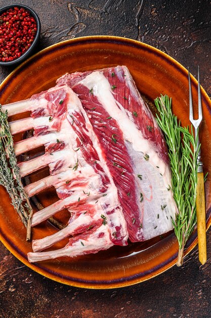 Carré di agnello fresco crudo con erbe verdi. Sfondo scuro. Vista dall'alto.