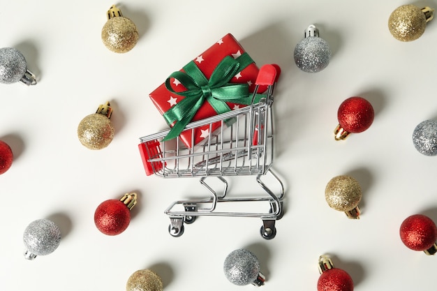 Carrello del negozio con scatola di Natale e bagattelle sul tavolo bianco