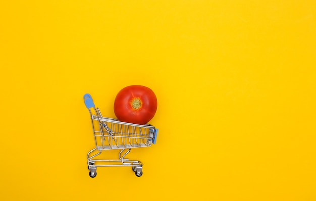 Carrello del supermercato con pomodoro su sfondo giallo.