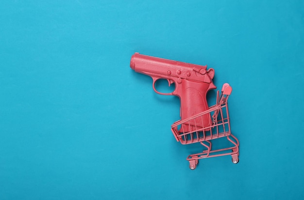 Carrello della spesa con pistola rosa su sfondo blu Layout minimalista creativo Idea fresca Concept art Vista dall'alto piatta