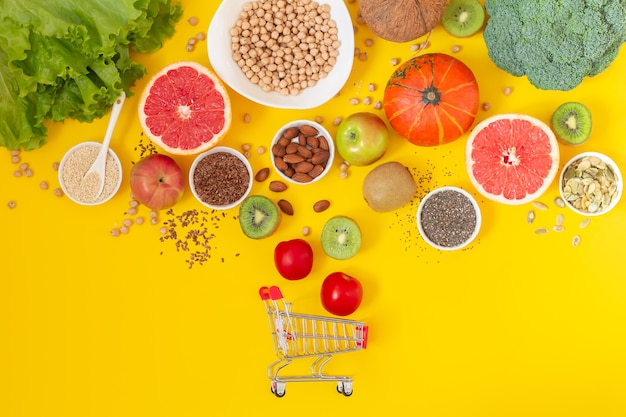 Carrello della spesa con verdure biologiche fresche, frutta e semi su sfondo giallo vista dall'alto