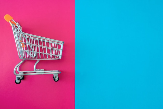 Carrello della spesa del supermercato self-service con sfondo rosa e blu.