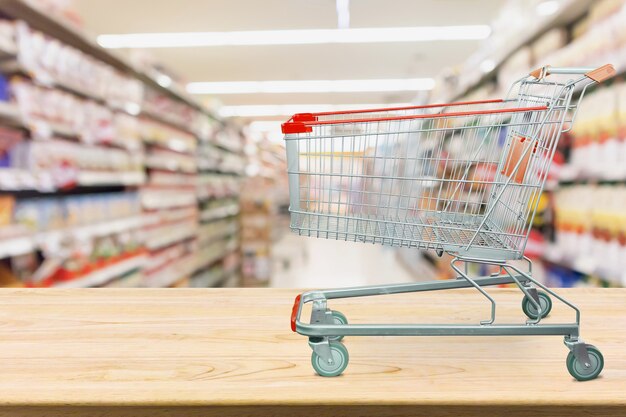 Carrello della spesa del supermercato sulla tavola di legno con fondo vago corridoio della drogheria