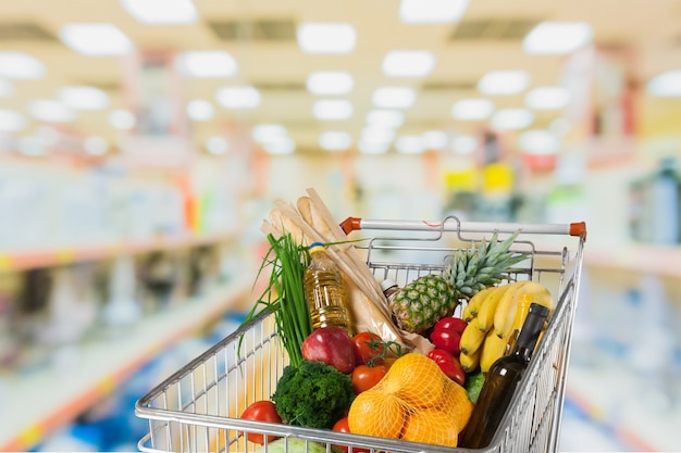 Carrello della spesa pieno con vari generi alimentari sullo sfondo