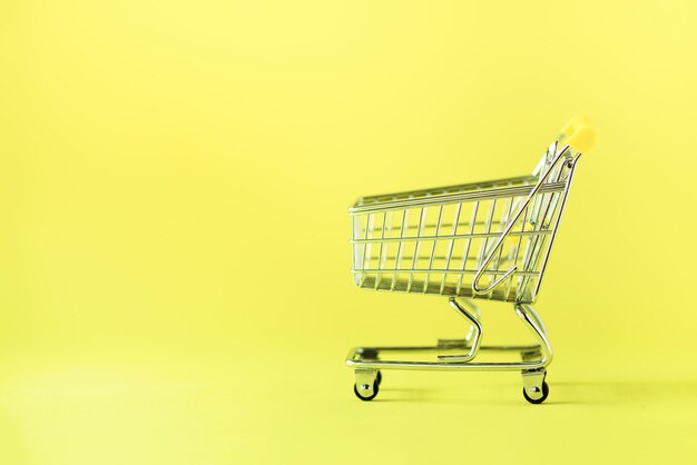 Carrello della spesa su sfondo giallo Stile minimalista Design creativo Copia spazio Carrello del negozio al supermercato Concetto di vendita sconto shopaholism Tendenza della società dei consumi