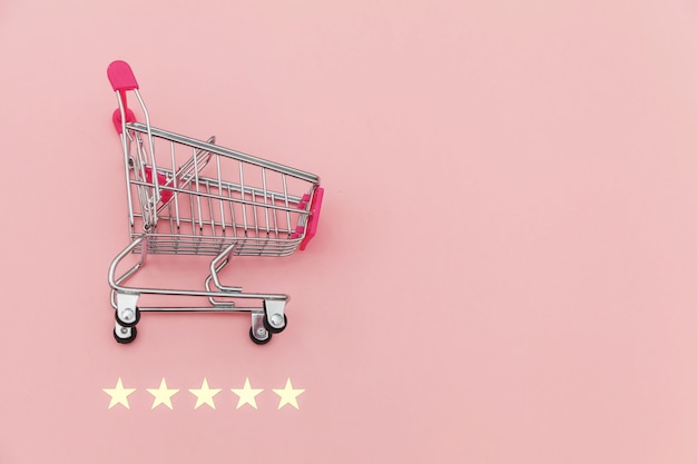 Carrello di spinta della piccola drogheria del supermercato per il giocattolo di compera con le ruote e una valutazione di 5 stelle isolata su fondo di rosa pastello. Consumatore al dettaglio che acquista concetto online di valutazione e recensione.