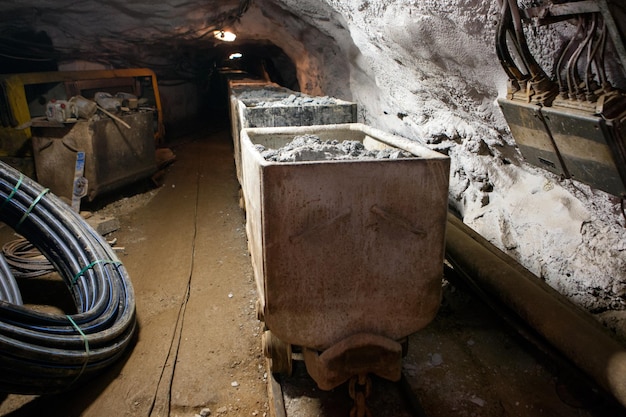 Carrello Hutch con materia prima in piedi all'estrazione sotterranea. Concetto di produzione e tecnologia. Tunnel con cavi ferroviari e miniera di elettricità di miniere sotterranee. Trasporto e illuminazione.