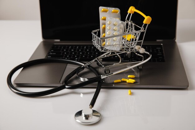 Carrello per farmacia online e consegna farmaci con pillole e stetoscopio su un laptop