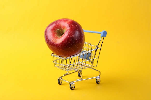 Carrello per supermercati con mela rossa su sfondo giallo