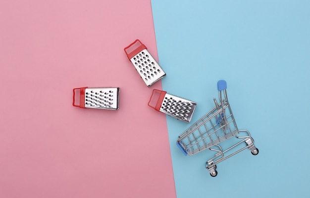 Carrello per supermercati con mini grattugie su sfondo rosa pastello blu. Vista dall'alto