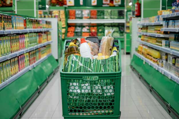 Carrello pieno di generi alimentari nelle verdure del supermercato sul concetto di consumismo di sfondo