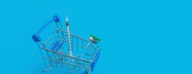 Carrello supermercato con siringhe e fiala su sfondo blu panorama