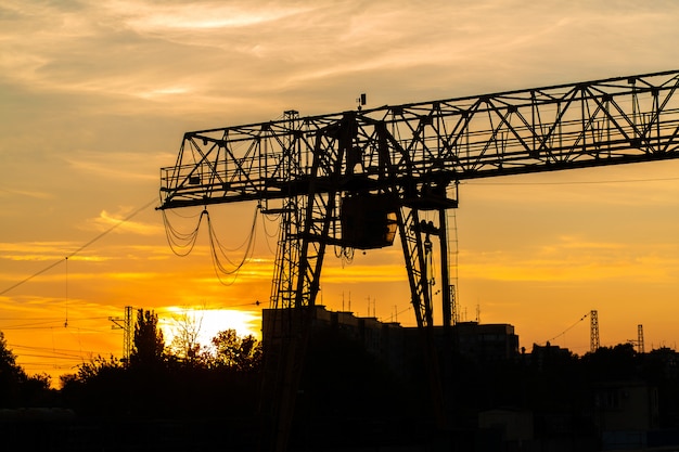 Carroponte alla stazione ferroviaria. Siluetta della gru su sfondo tramonto. Concetto di industria pesante.