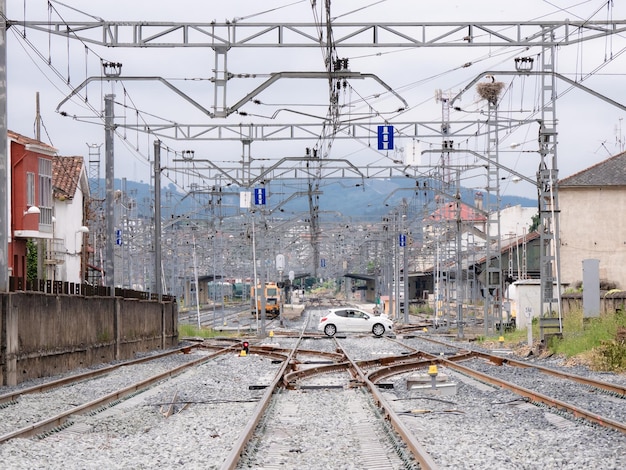 Carrozza bianca che attraversa un passaggio a livello sui binari del treno all'ingresso della stazione di Monforte de Lemos sotto i cavi della catenaria e la stazione sullo sfondo