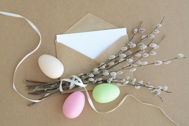 Carta bianca colorata uova di pasqua rami di salice e busta di carta artigianale su uno sfondo di cartone