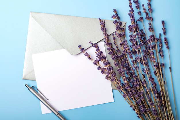 Carta bianca con busta e fiori di lavanda su sfondo blu. Carta di matrimonio semplice. Vista dall'alto
