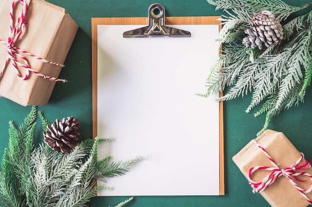 Carta bianca con scatole regalo e rami di albero di Natale su sfondo verde.