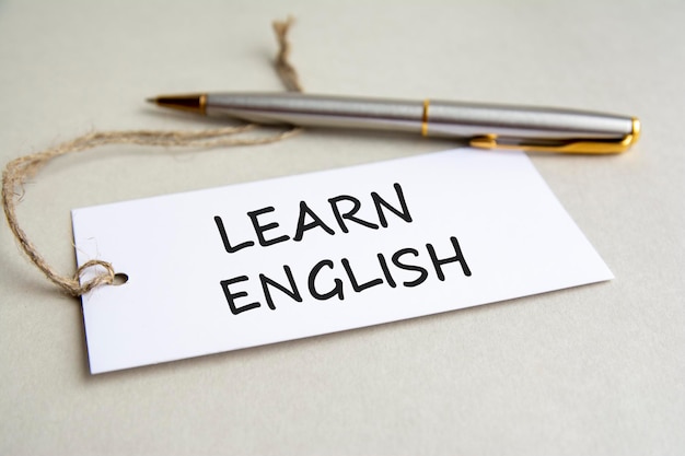 Carta bianca con testo Impara l'inglese con penna di metallo su sfondo grigio