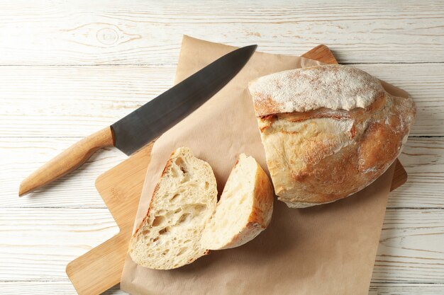 Carta da forno con pane e coltello su fondo di legno bianco