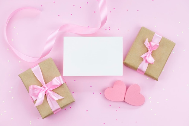 Carta di carta bianca mock up su sfondo rosa con regali nastro rosa e due cuori
