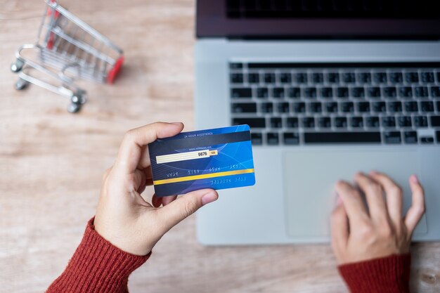 Carta di credito d'uso della tenuta del maglione della donna e computer portatile usando per l'acquisto online