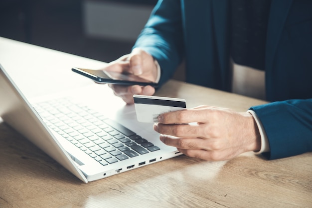 Carta di credito della mano dell'uomo con il telefono e il computer sul tavolo