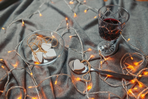 Carta di San Valentino. Cuori di legno bianchi su sfondo grigio. Cuori con ghirlande e bicchiere di vino.