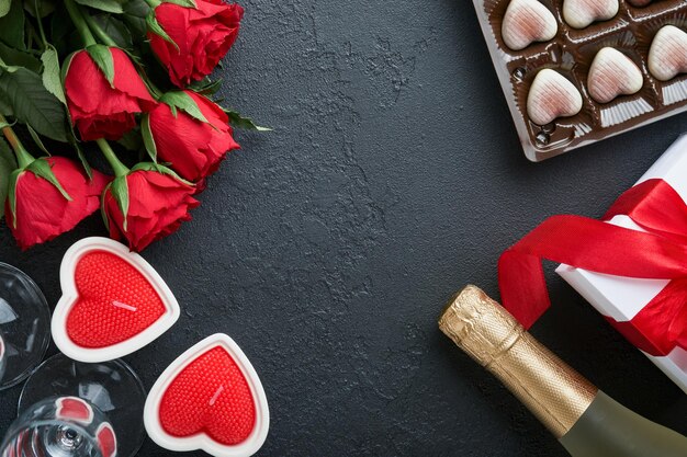 Carta di San Valentino Fiori rossi rosa biscotti brownie e caramelle al cioccolato su confezione regalo a forma di cuore con vino su sfondo nero Biglietto di auguri per la festa della mamma o della donna Vista dall'alto piatto