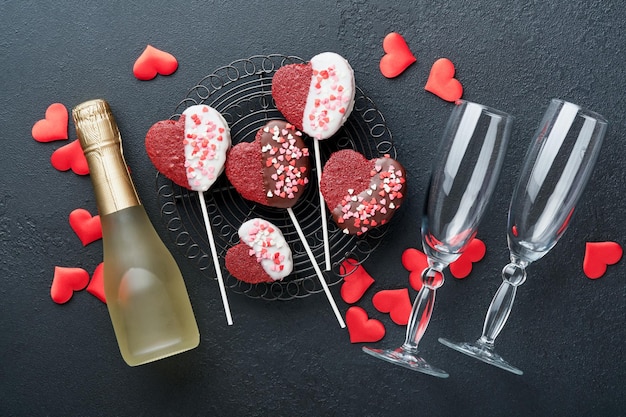 Carta di San Valentino Fiori rossi rosa biscotti brownie e caramelle al cioccolato su confezione regalo a forma di cuore con vino su sfondo nero Biglietto di auguri per la festa della mamma o della donna Vista dall'alto piatto