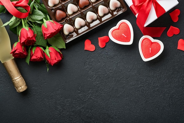 Carta di San Valentino Fiori rossi rosa biscotti brownie e caramelle al cioccolato su confezione regalo a forma di cuore con vino su sfondo nero Biglietto di auguri per la festa della mamma o della donna Vista dall'alto piatto