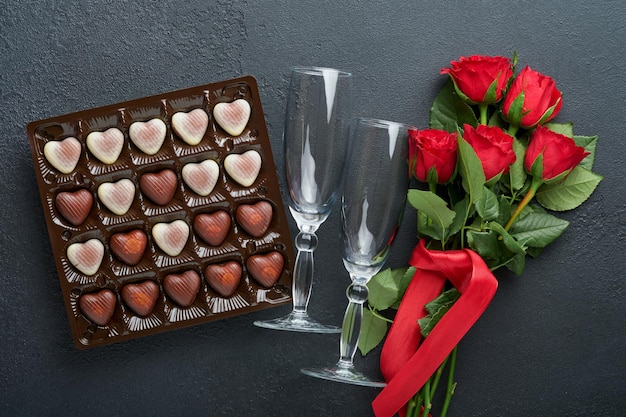 Carta di San Valentino Fiori rossi rosa biscotti brownie e caramelle al cioccolato su confezione regalo a forma di cuore con vino su sfondo nero Biglietto di auguri per la festa della mamma o della donna Vista dall'alto piatto